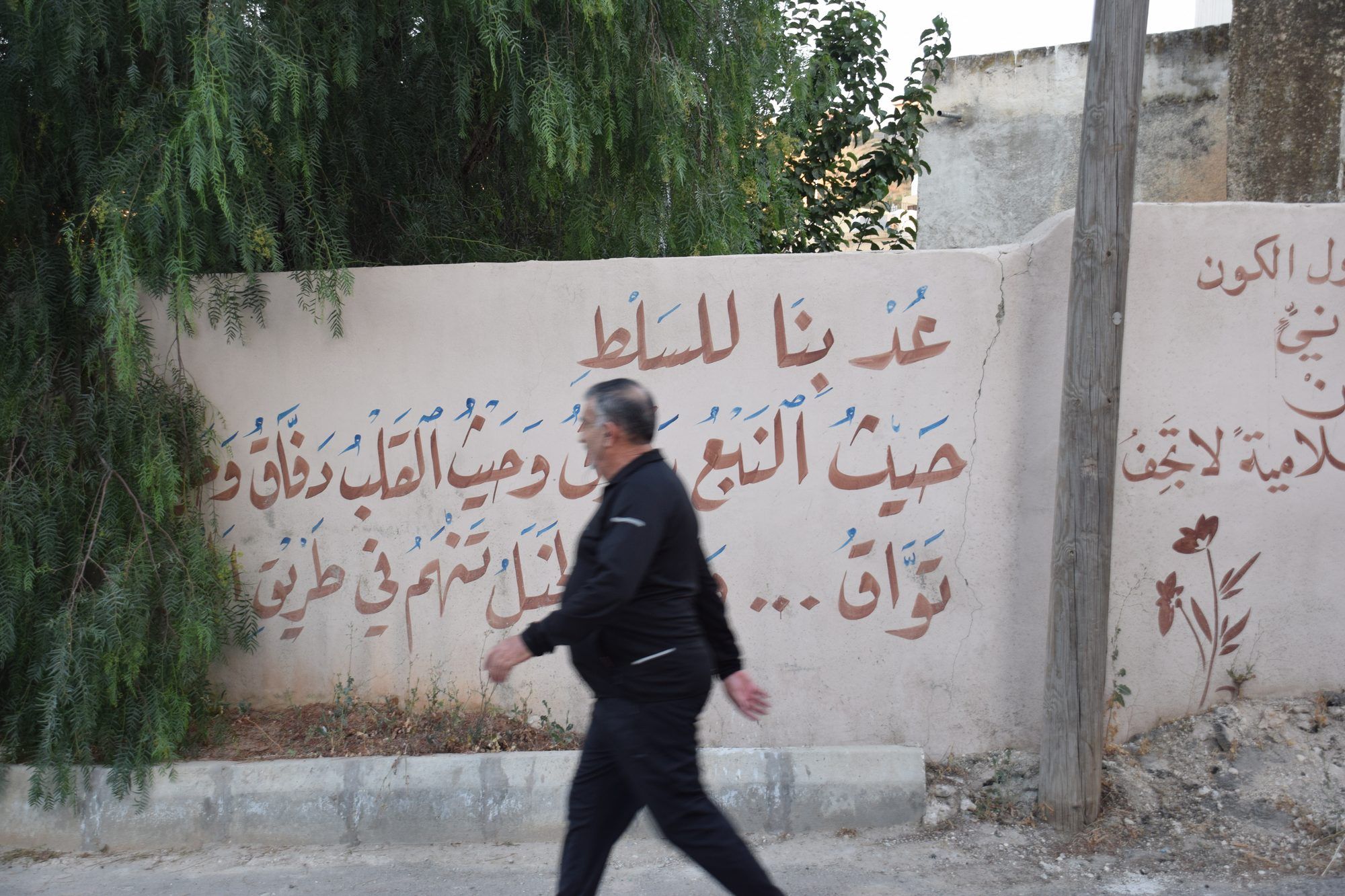 رجل يمشي بجانب جدار مكتوب عليه شعر عربي