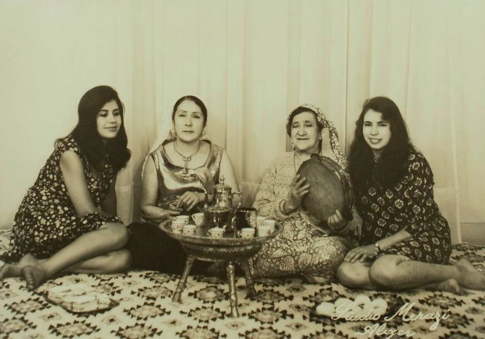 Cheikha Rimitti seated with other women around a tea tray and a frame drum